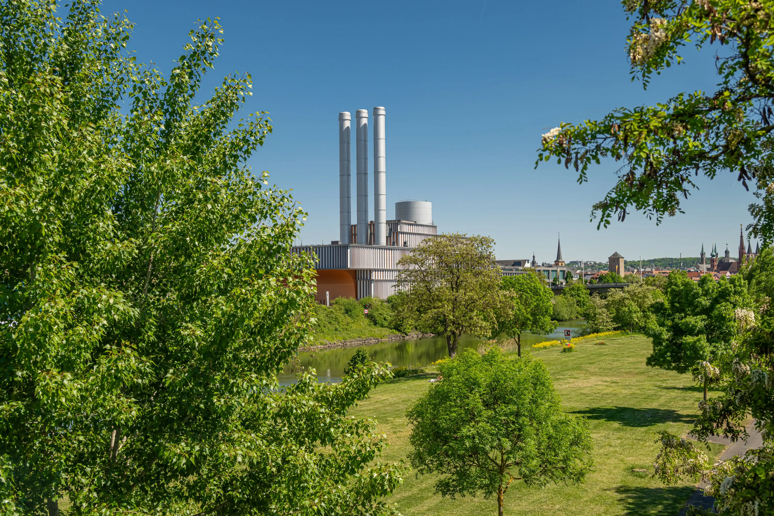 Heizkraftwerk Würzburg mit drei Schornsteinen hinter grünen Bäumen
