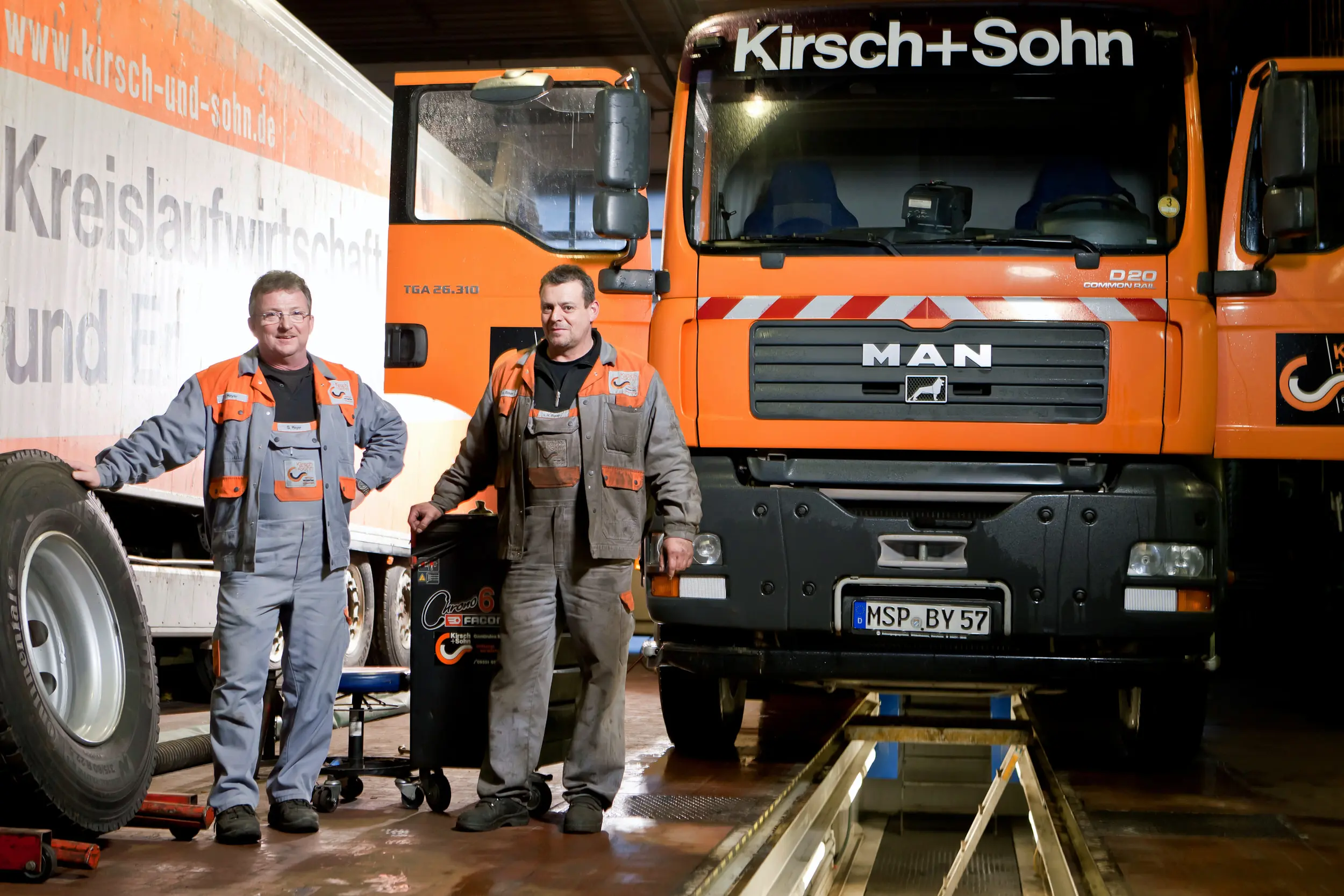 Zwei Mitarbeiter in Arbeitskleidung vor einem Lkw von Kirsch und Sohn