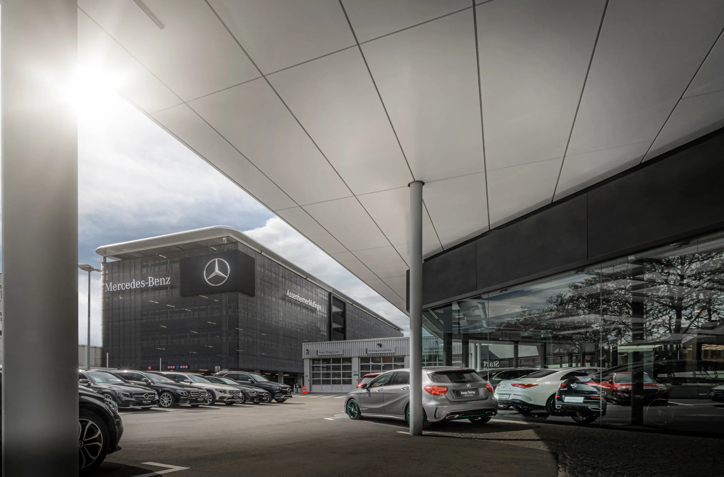 Blick unter dem Vordach auf Verkaufsgebäude und Parkplatz eines Mercedes-Benz-Autohauses