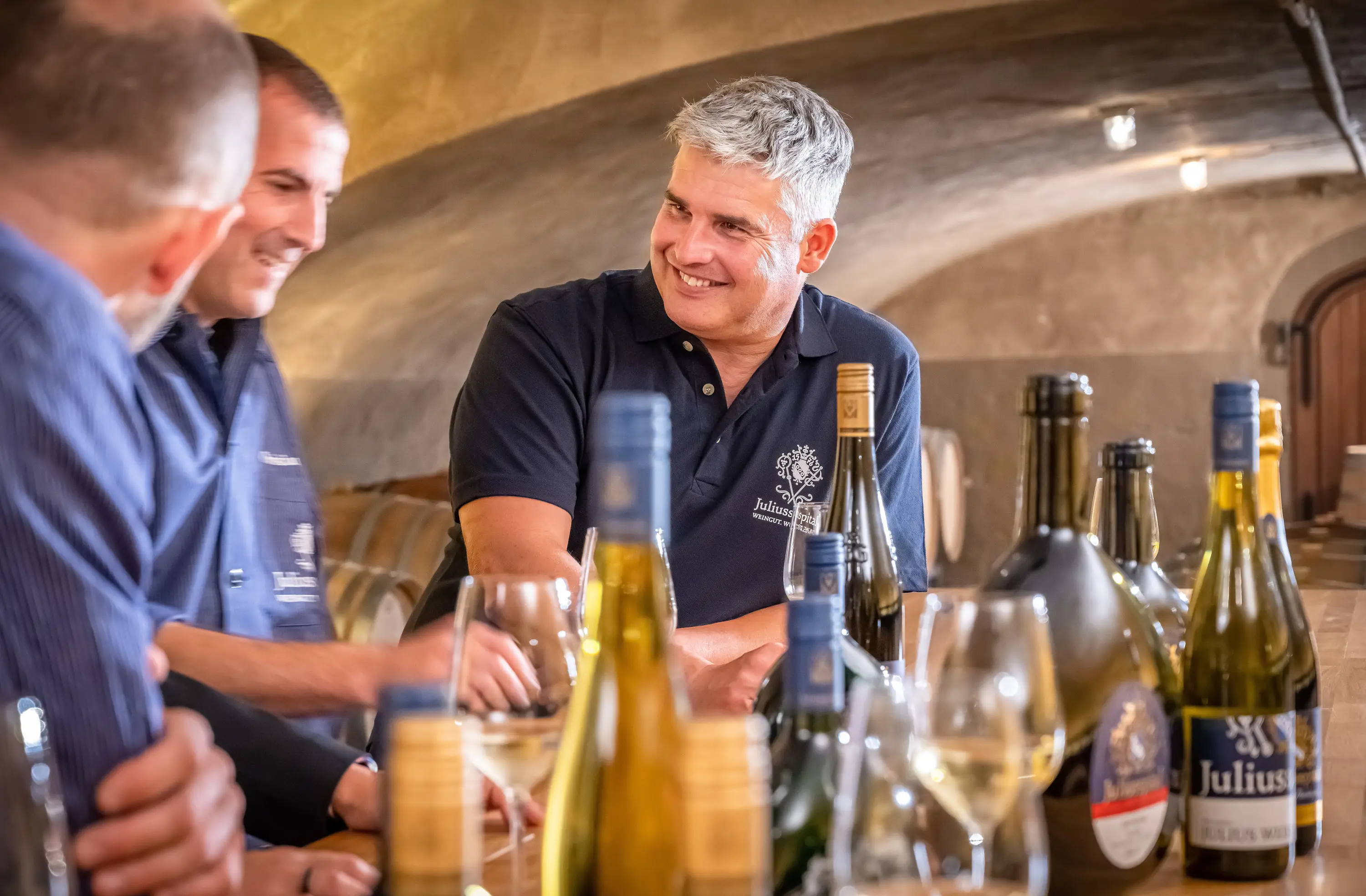 Kellermeister und Winzer lachen bei der Weinprobe am Tresen, Juliusspital Würzburg