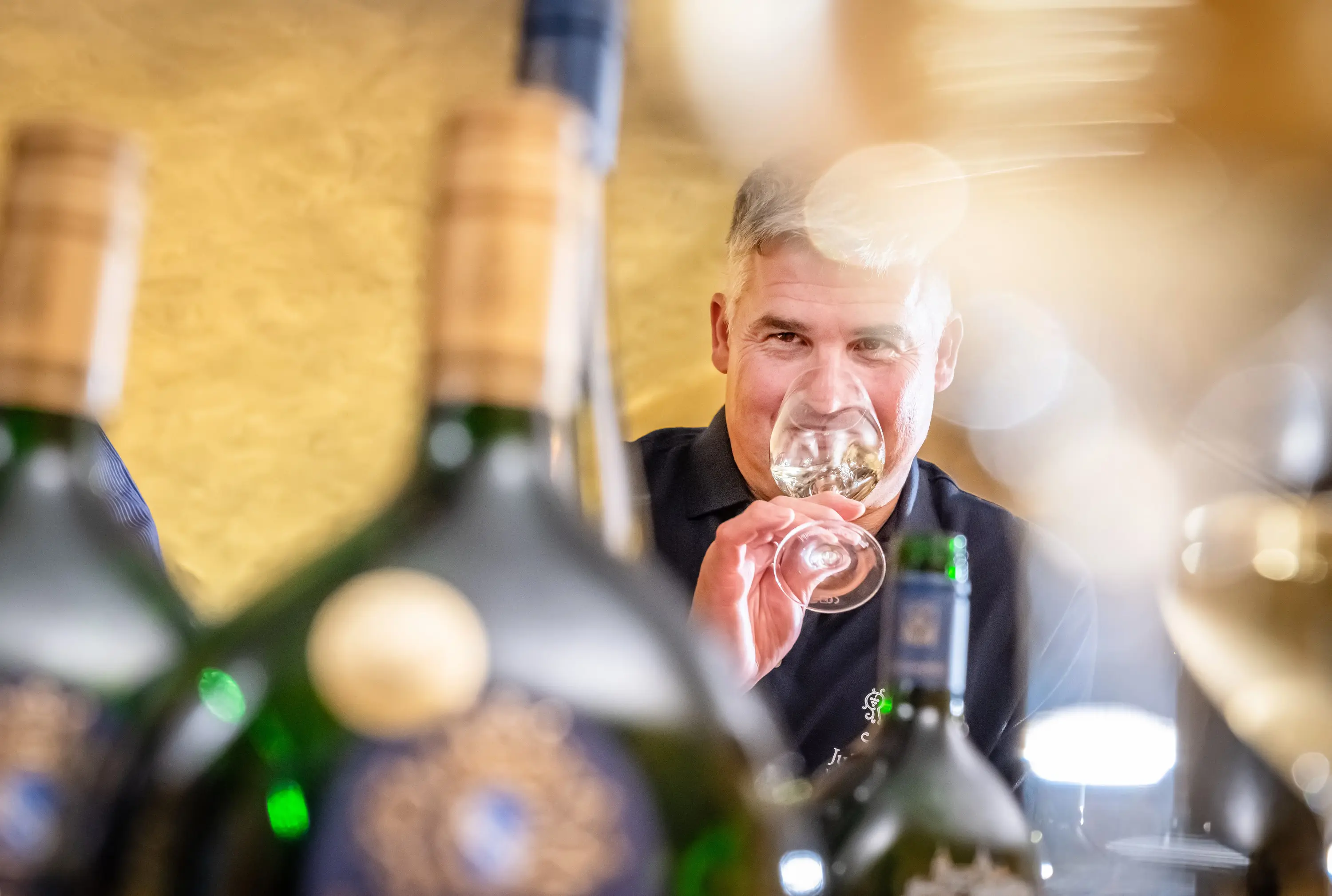 Kellermeister prüft den Duft eines Weißweins hinter Weinflaschen, Juliusspital Würzburg